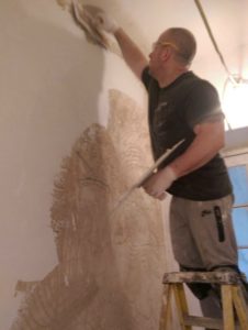 A man on a step ladder plastering a wall in a hallway.In Bristol, England